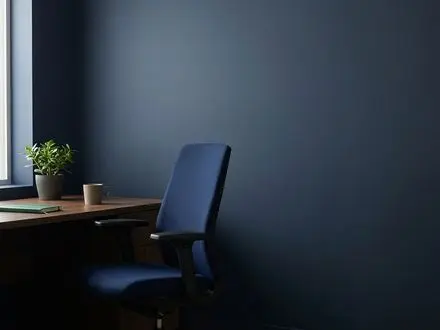 Empty modern office chair beside a tidy desk in a small business office, in deep navy and green tones, conveying a vacant role and employee turnover.
