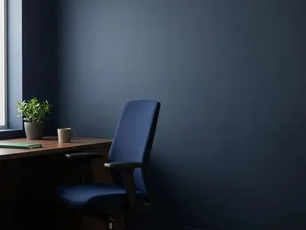 Empty modern office chair beside a tidy desk in a small business office, in deep navy and green tones, conveying a vacant role and employee turnover.