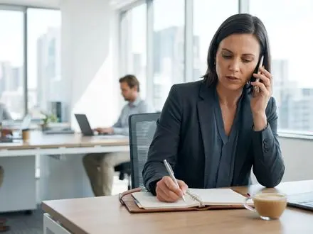 Hiring manager on a phone screen call taking notes at a desk